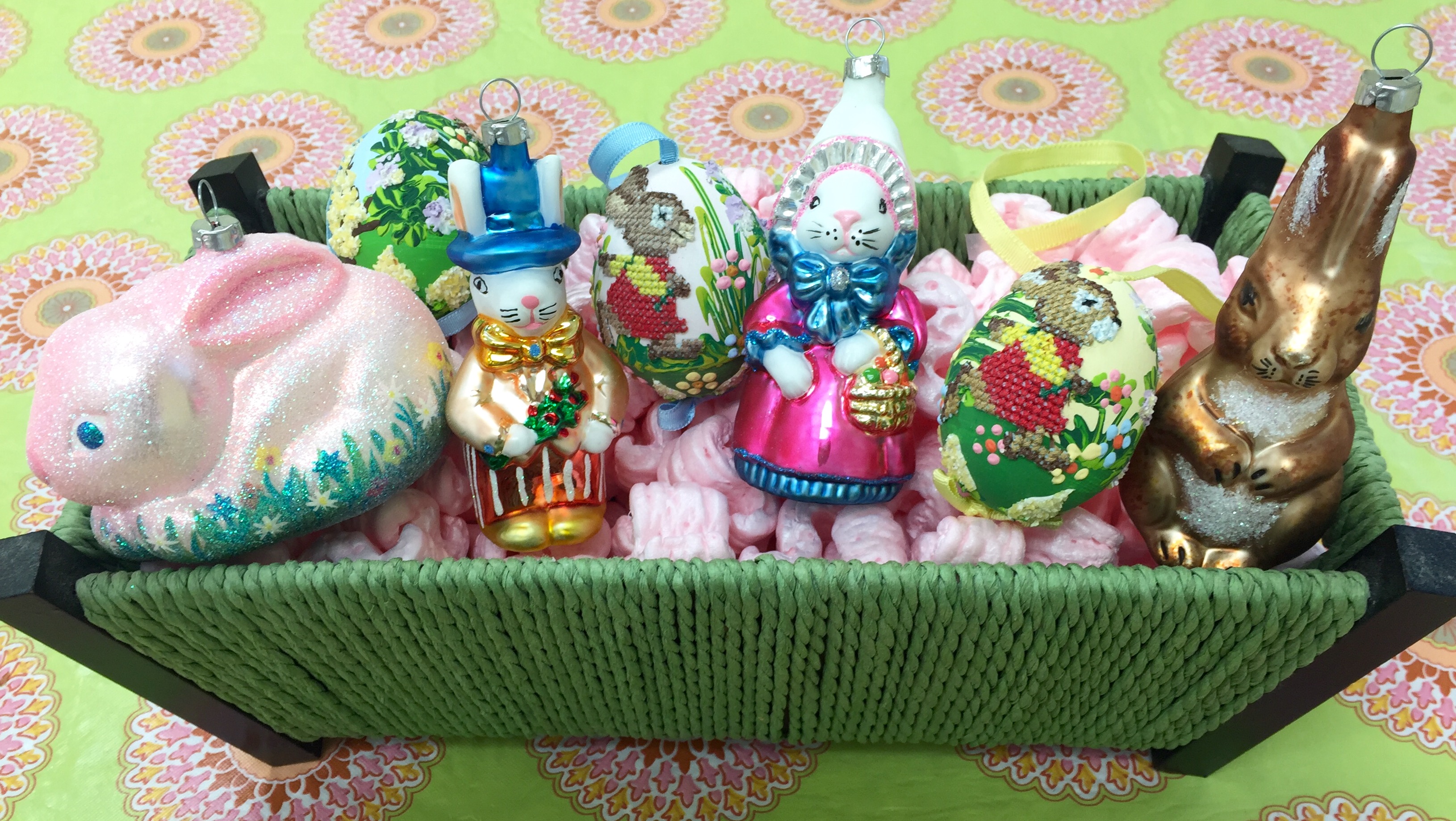 A basket full of Easter ornaments contains a pink sparkled bunny, a colorful bunny couple, a set of 3 needle point egg ornaments, and a brown forest bunny ornament | OrnamentShop.com