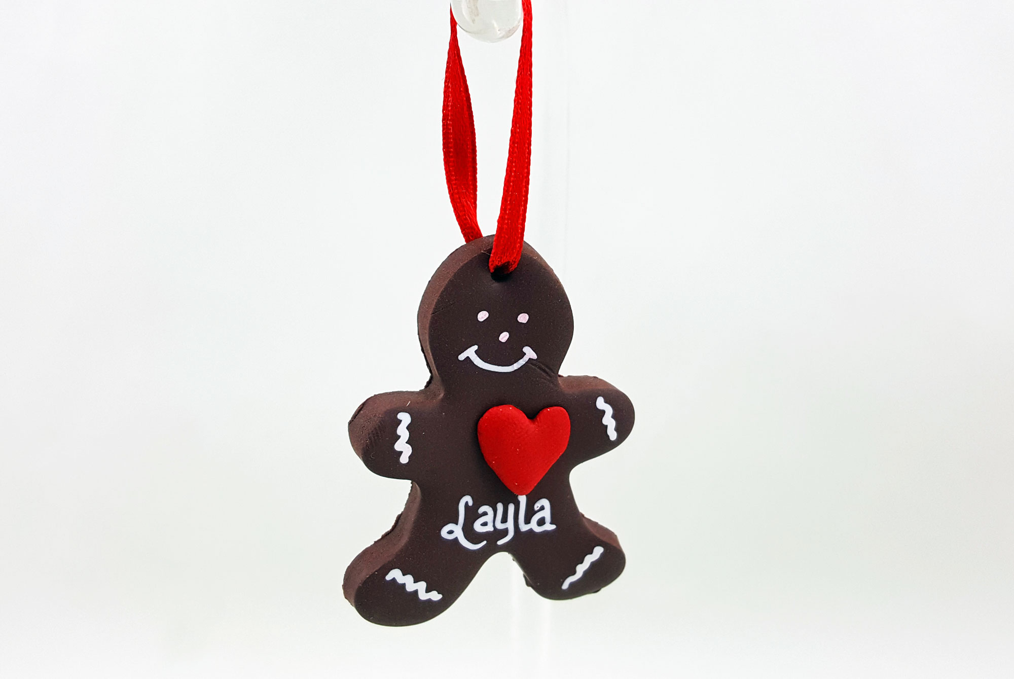 A DIY gingerbread man ornament with a red heart and white features, hung with a red ribbon | Ornamentshop.com