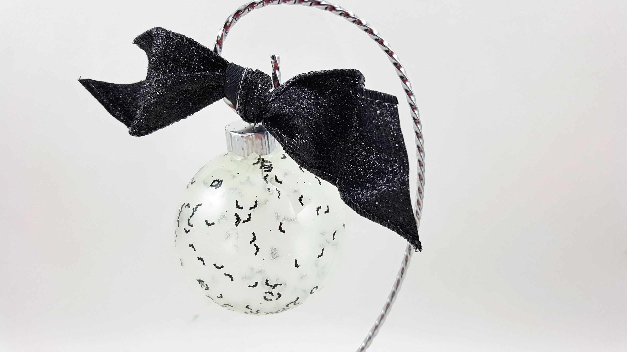 A DIY Halloween ornament that rests on it's own stand, made of a clear glass ball, glow in the dark nail polish, plastic confetti and a ribbon. | OrnamentShop.com