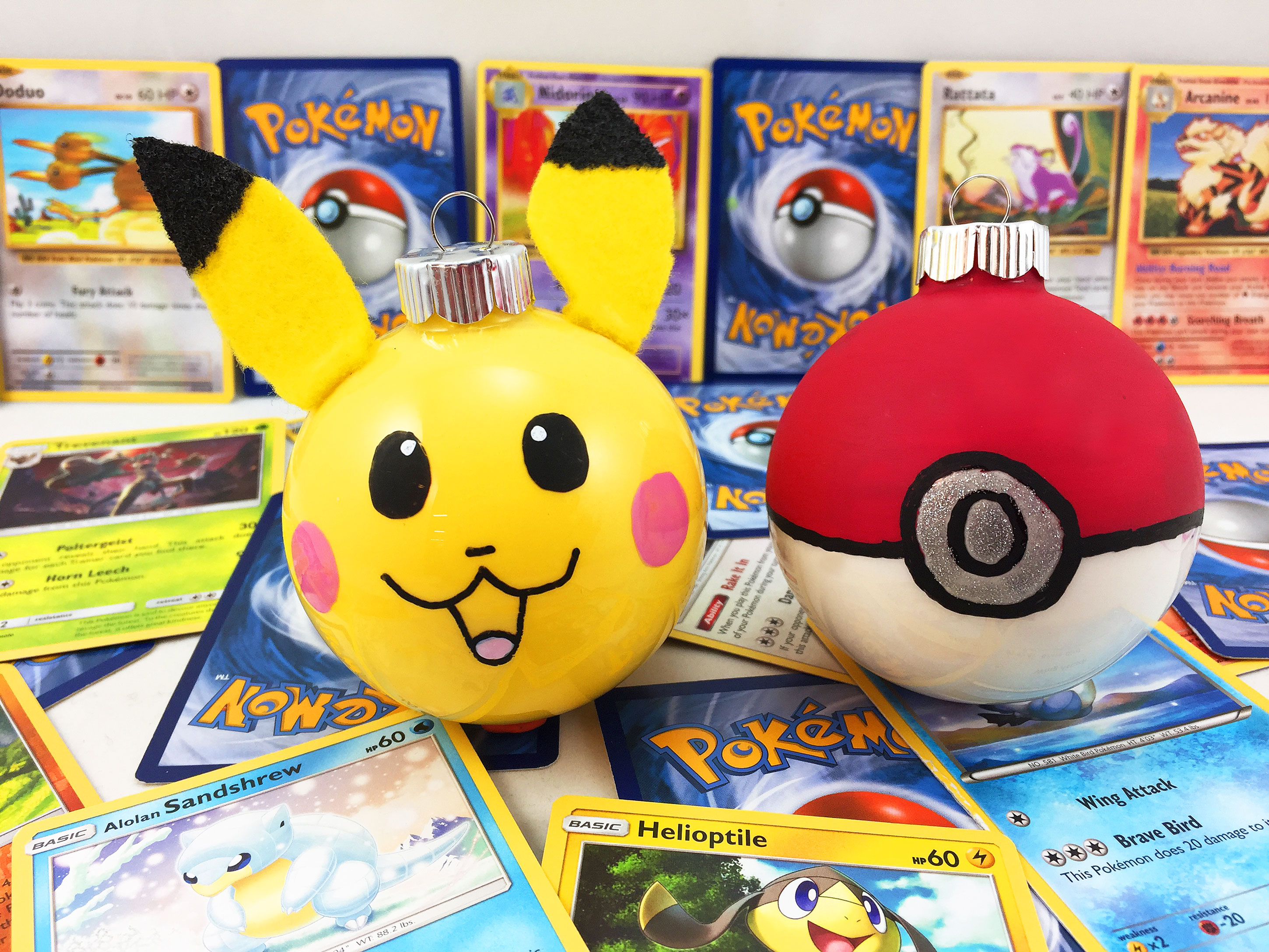 Two DIY Pokemon ornaments are surrounded by a Pokemon fan's trading card collection. | OrnamentShop.com