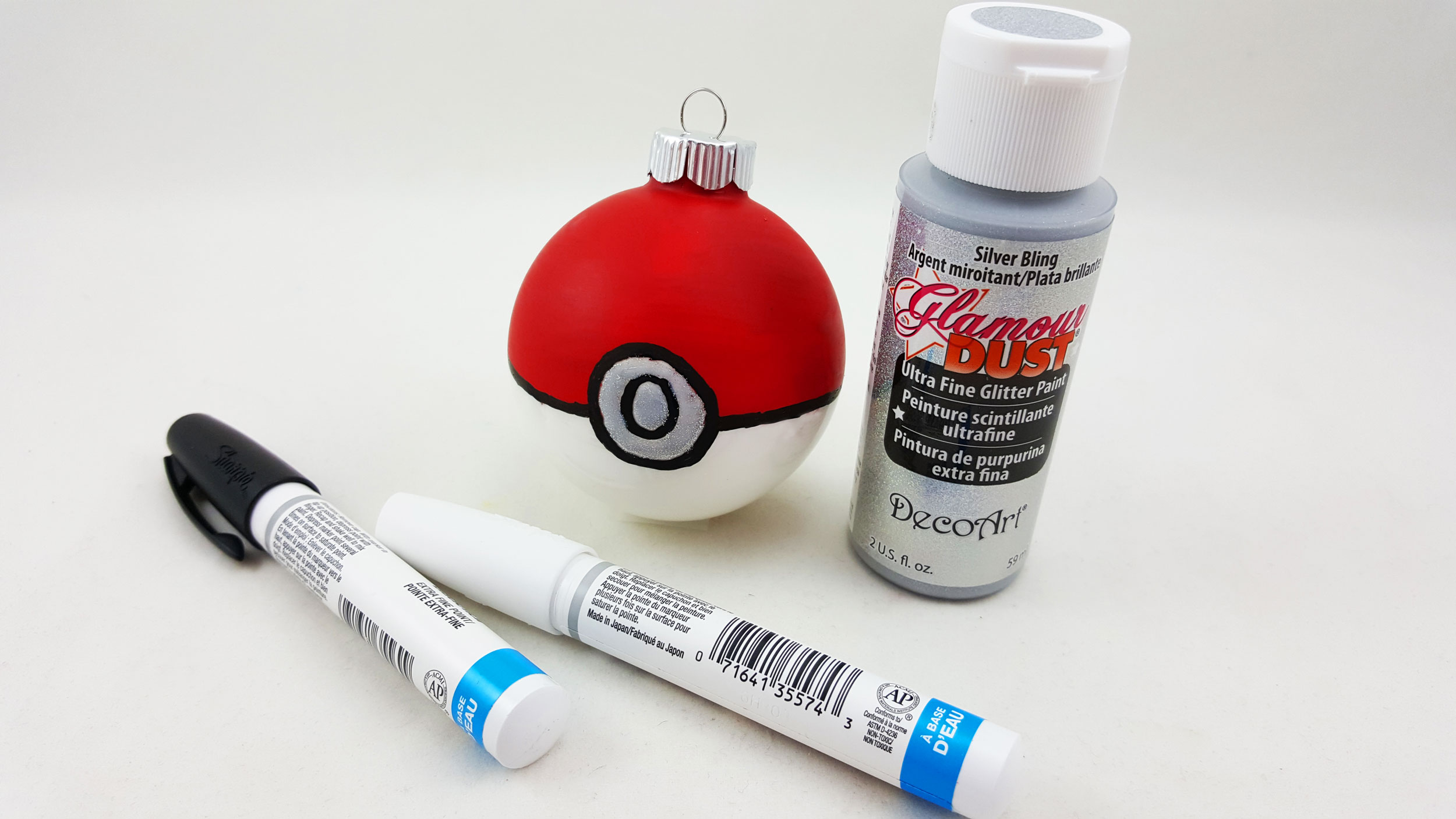 The third and final step to make a Pokeball ornament is to use the black paint market to draw a line across the hemisphere of the ball and the circle on the front. Use silver glitter paint to add a shiny detail to the circle on the front. | OrnamentShop.com