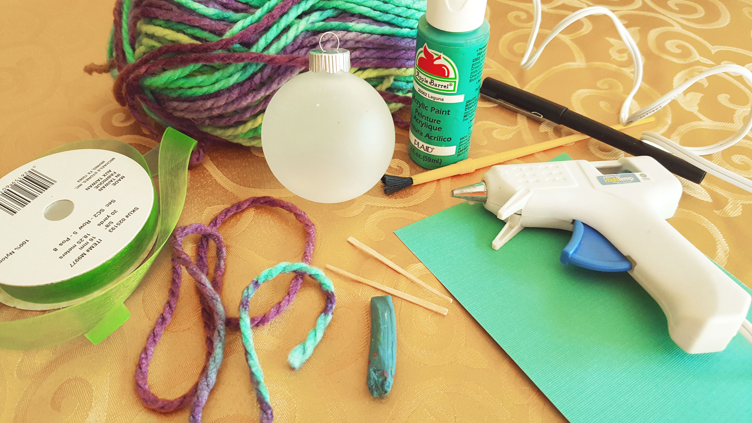 A list of supplies for a DIY yarn ornament including a glass ball ornament, yarn, a glue gun, toothpicks and a ribbon. | OrnamentShop.com