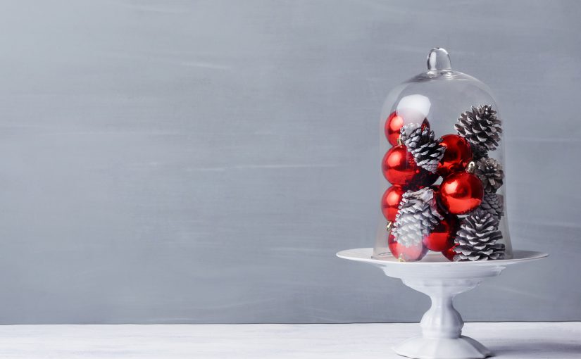 A glass cloche sits on a table filled with red baubles and pine cones for a Christmas theme. | OrnamentShop.com