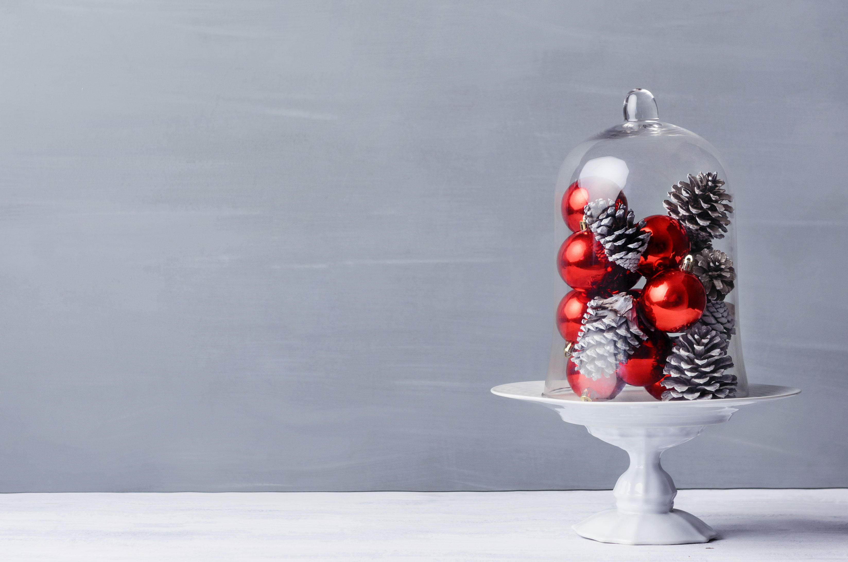 A glass cloche sits on a table filled with red baubles and pine cones for a Christmas theme. | OrnamentShop.com