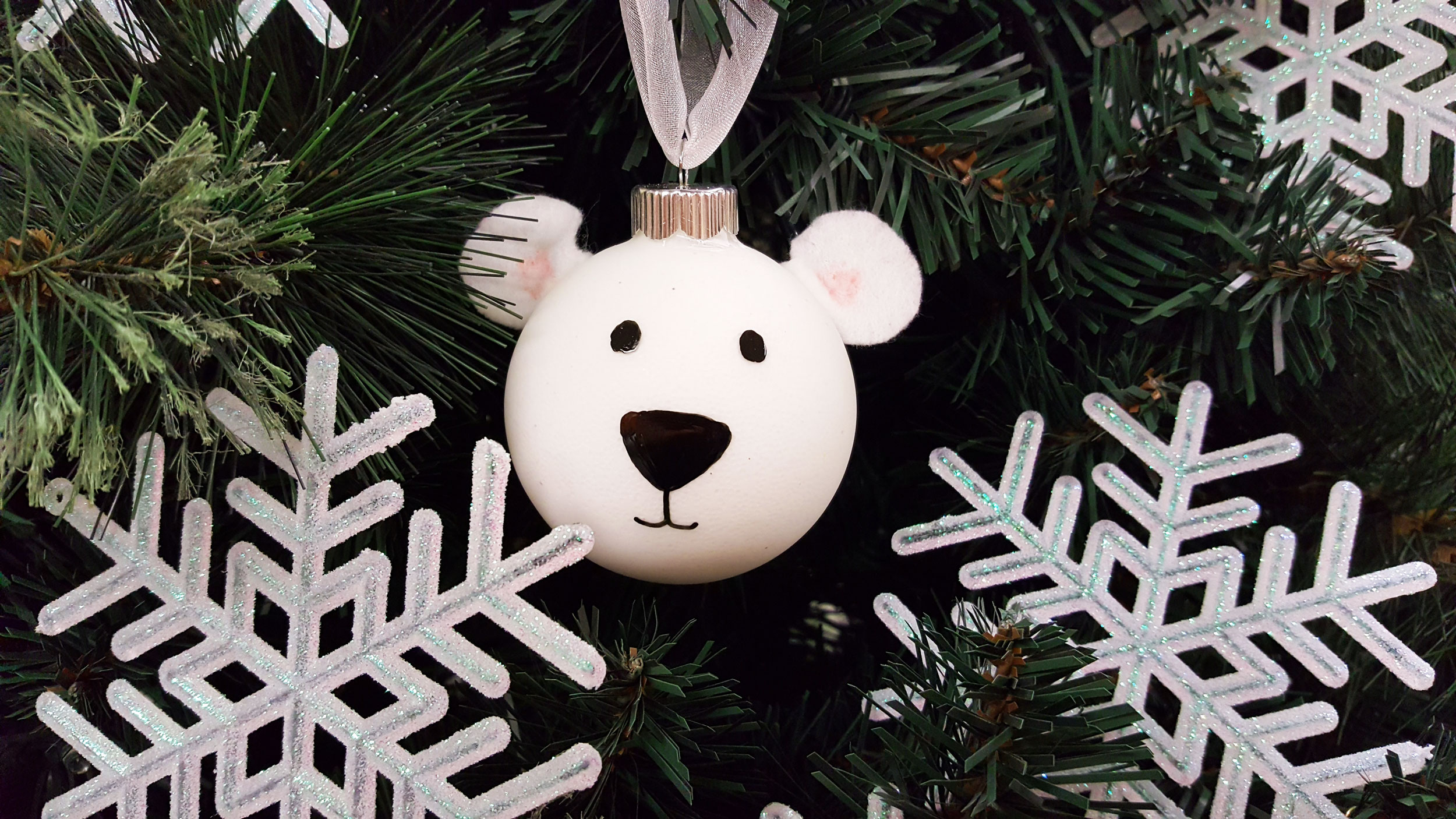 a white DIY polar bear ornament made from a bauble ornament and hiding in a tree behind giant snowflakes. | OrnamentShop.com