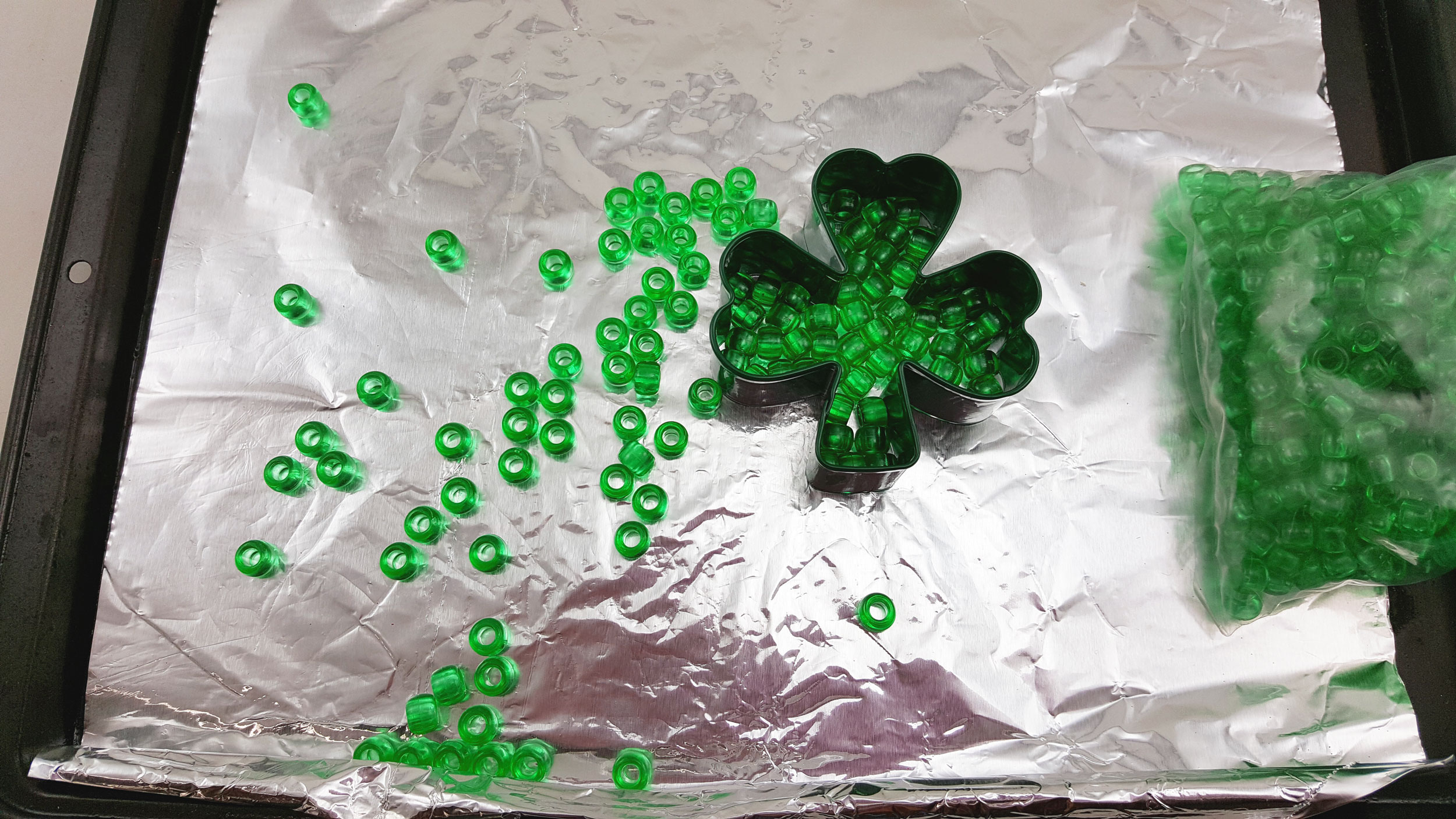 Step 1 is to place your metal clover cookie cutter on the foil and fill it with beads. | OrnamentShop.com