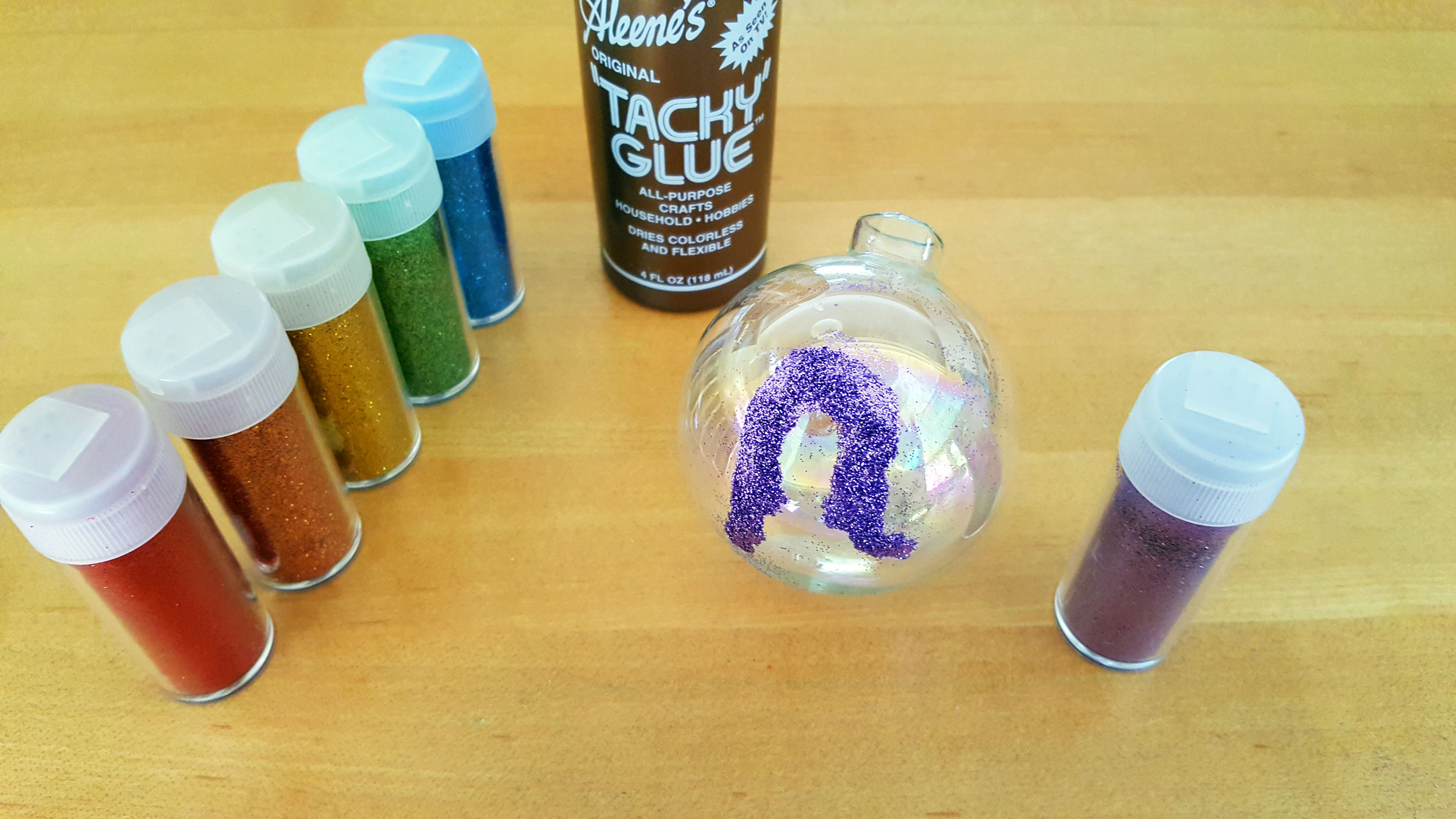 Step 1: Draw the innermost arch using a thin coat of glue to the glass ball, and then shake the purple glitter to cover the glue. | OrnamentShop.com