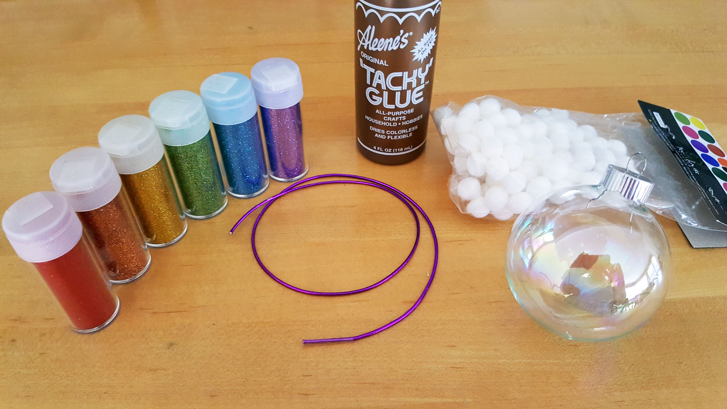 Supplies needed for the Glitter Rainbow Ornament: a Clear glass ball ornament, Rainbow colored glitter (Red, Orange, Yellow, Green, Blue, Violet), Glue, White pompoms or cotton balls, Ribbon or string, and Scissors | OrnamentShop.com