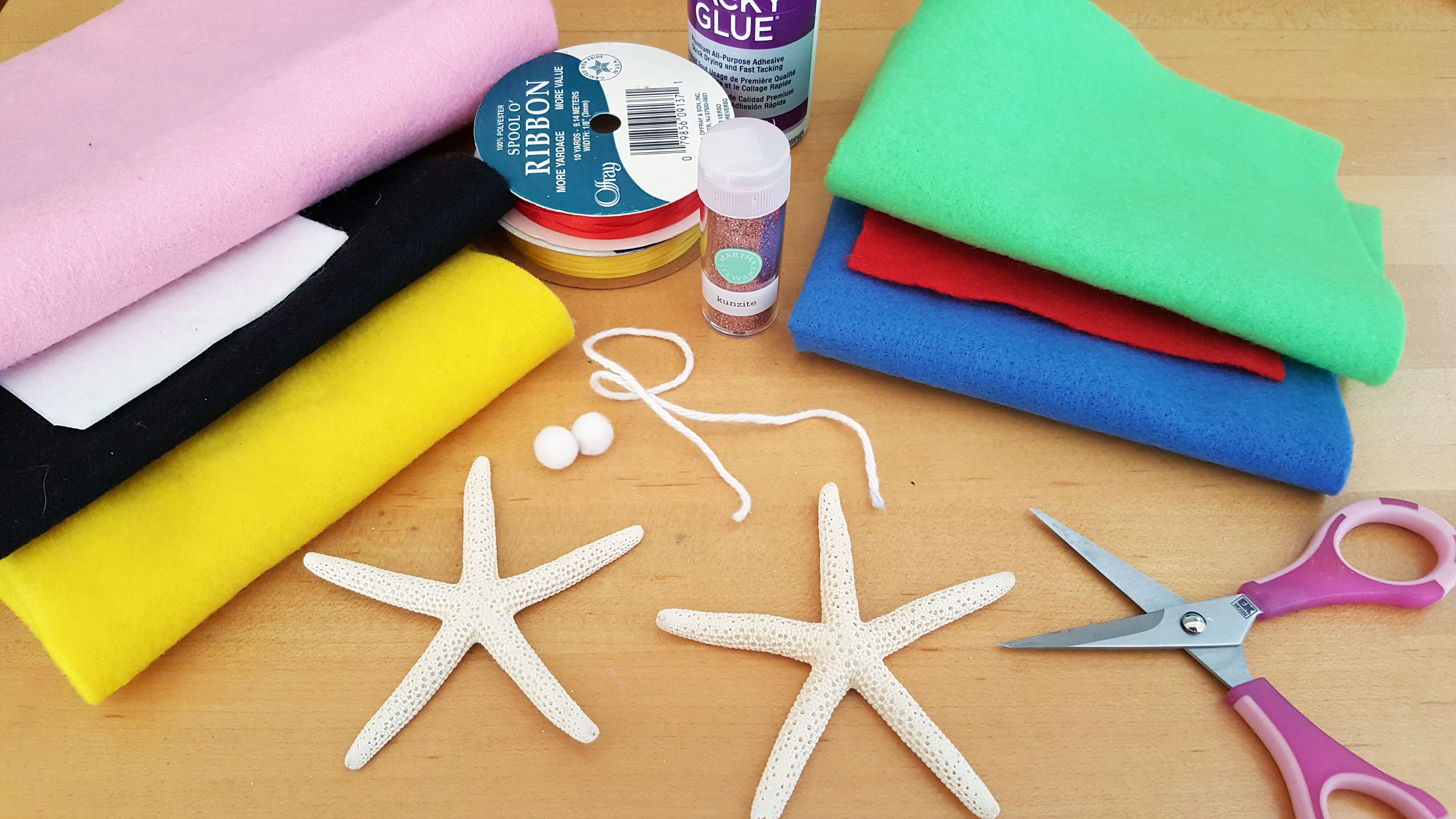 Felt in various colors, two starfish, sewing scissors, ribbon, and tacky glue on a wooden table. | OrnamentShop.com