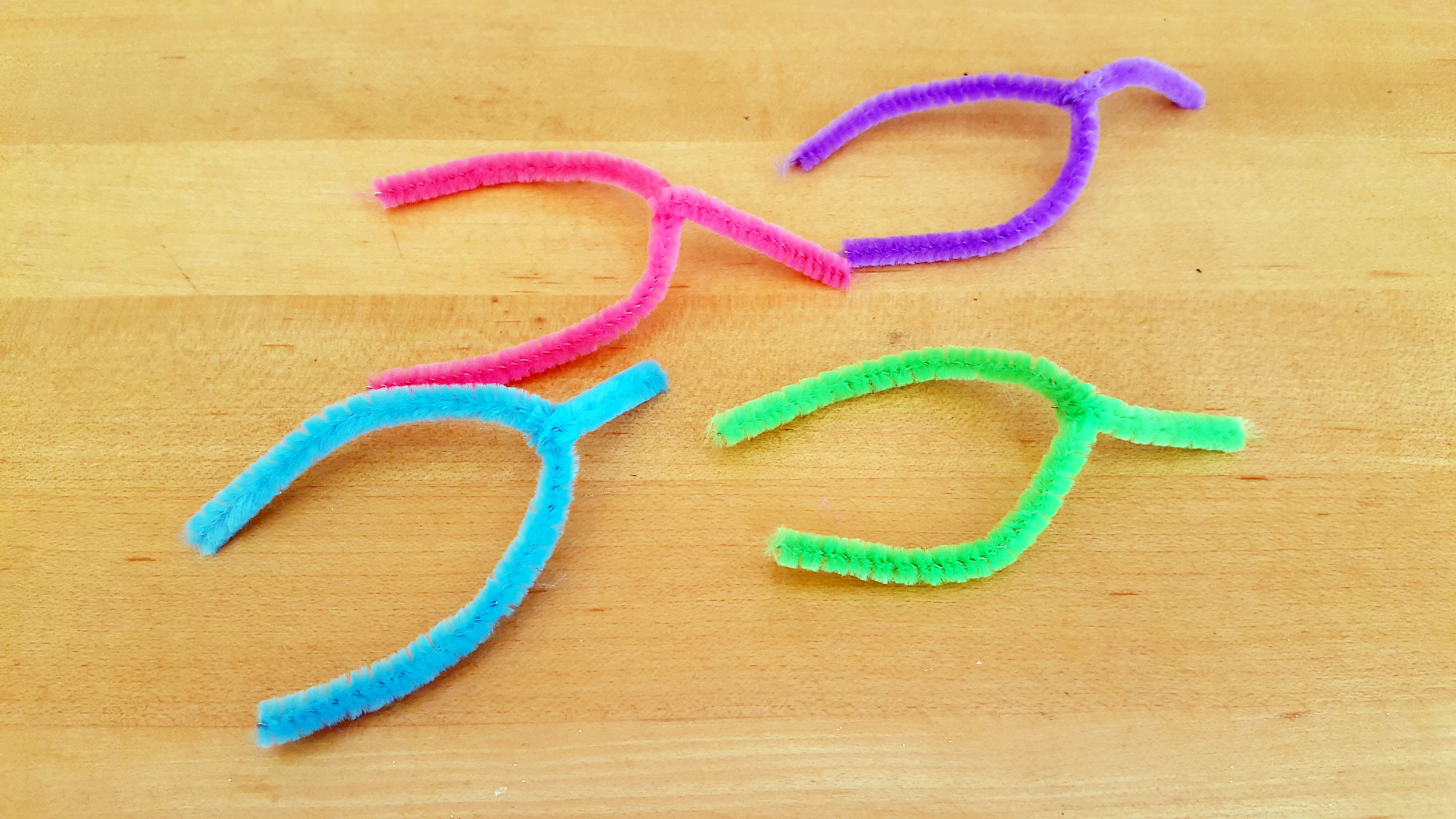 4 colorful pieces of pipe cleaners bent into arches placed on a table. | OrnamentShop.com