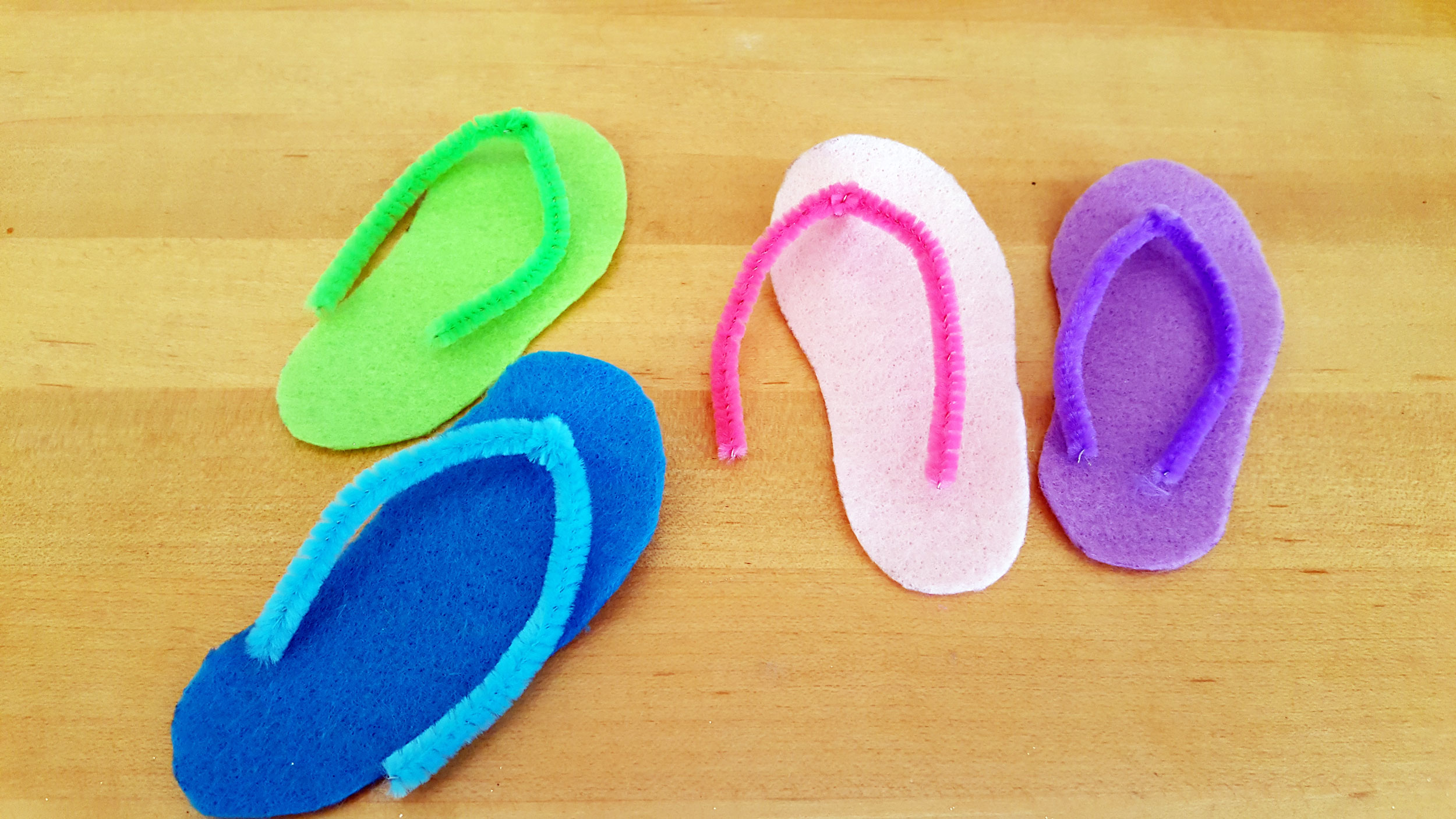 4 colorful arched pieces of pipe cleaners on top of 4 colorful shapes of felt cut into flip flop shapes. | OrnamentShop.com