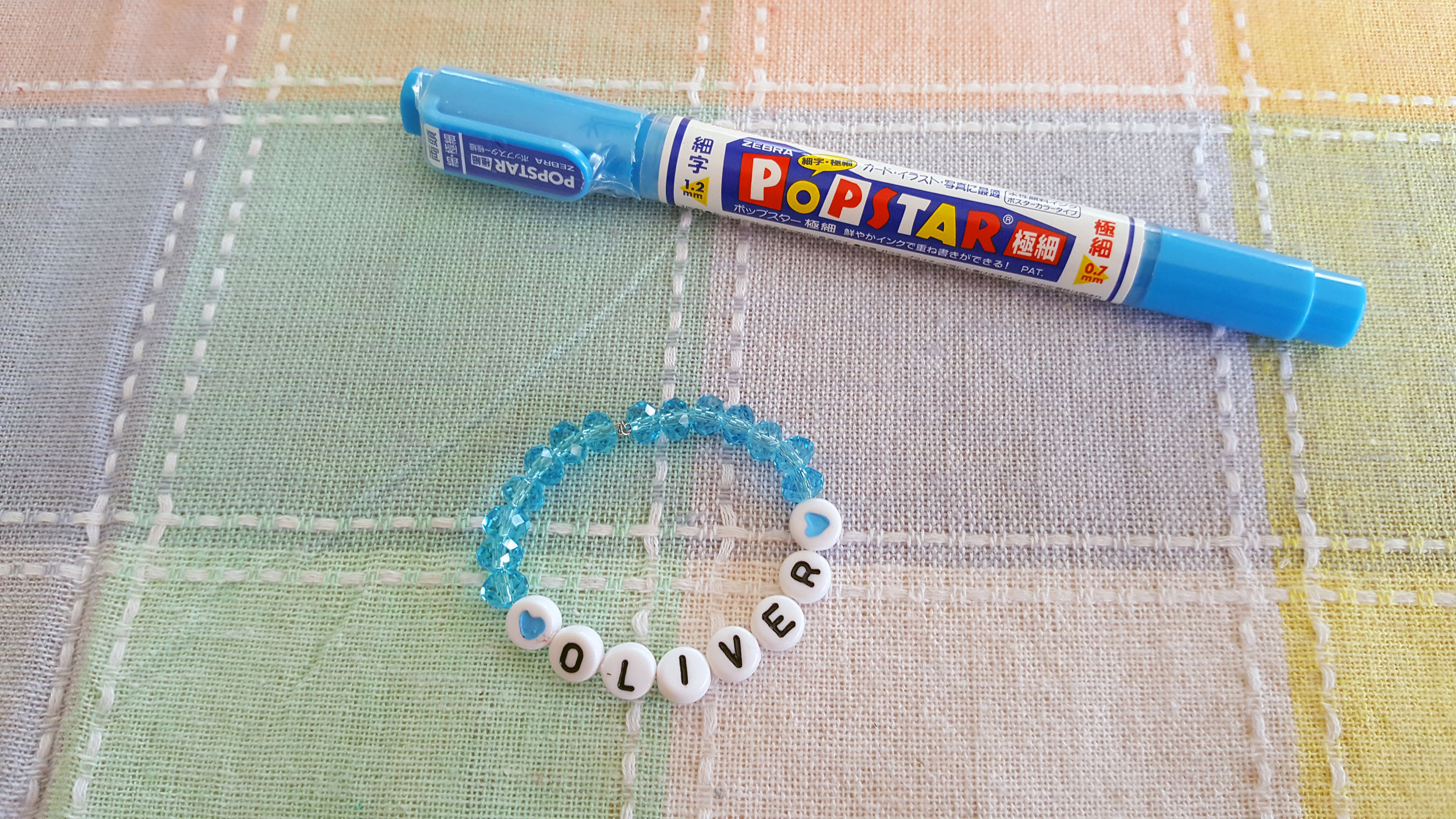 Newborn's name in beads (bracelet) and blue paint marker on table. | OrnamentShop.com