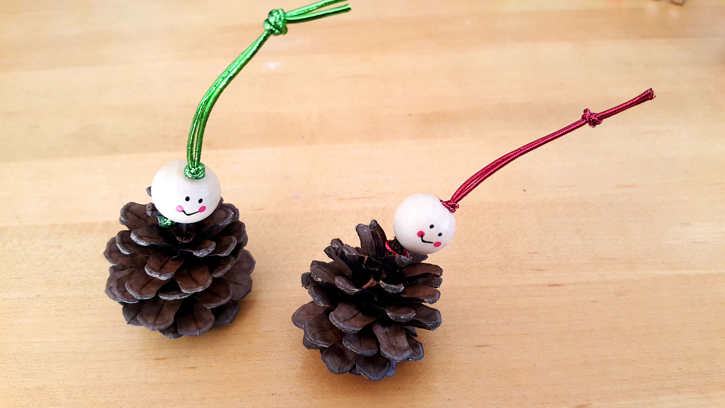 Pine Cone Elf Ornaments Step 2: Thread the head bead over the two ends of the string and tie a knot. | OrnamentShop.com