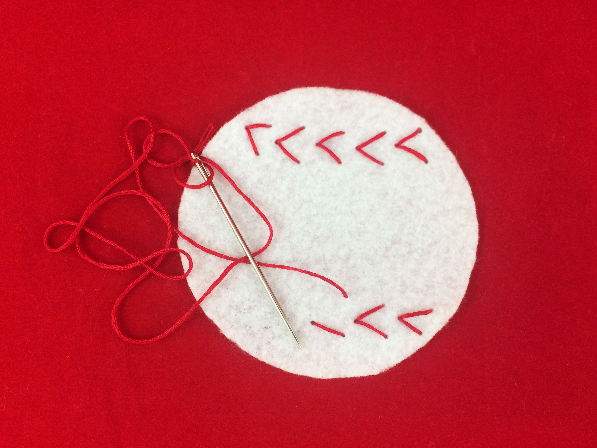 Red "V"s sewn with string on white felt circle. | OrnamentShop.com