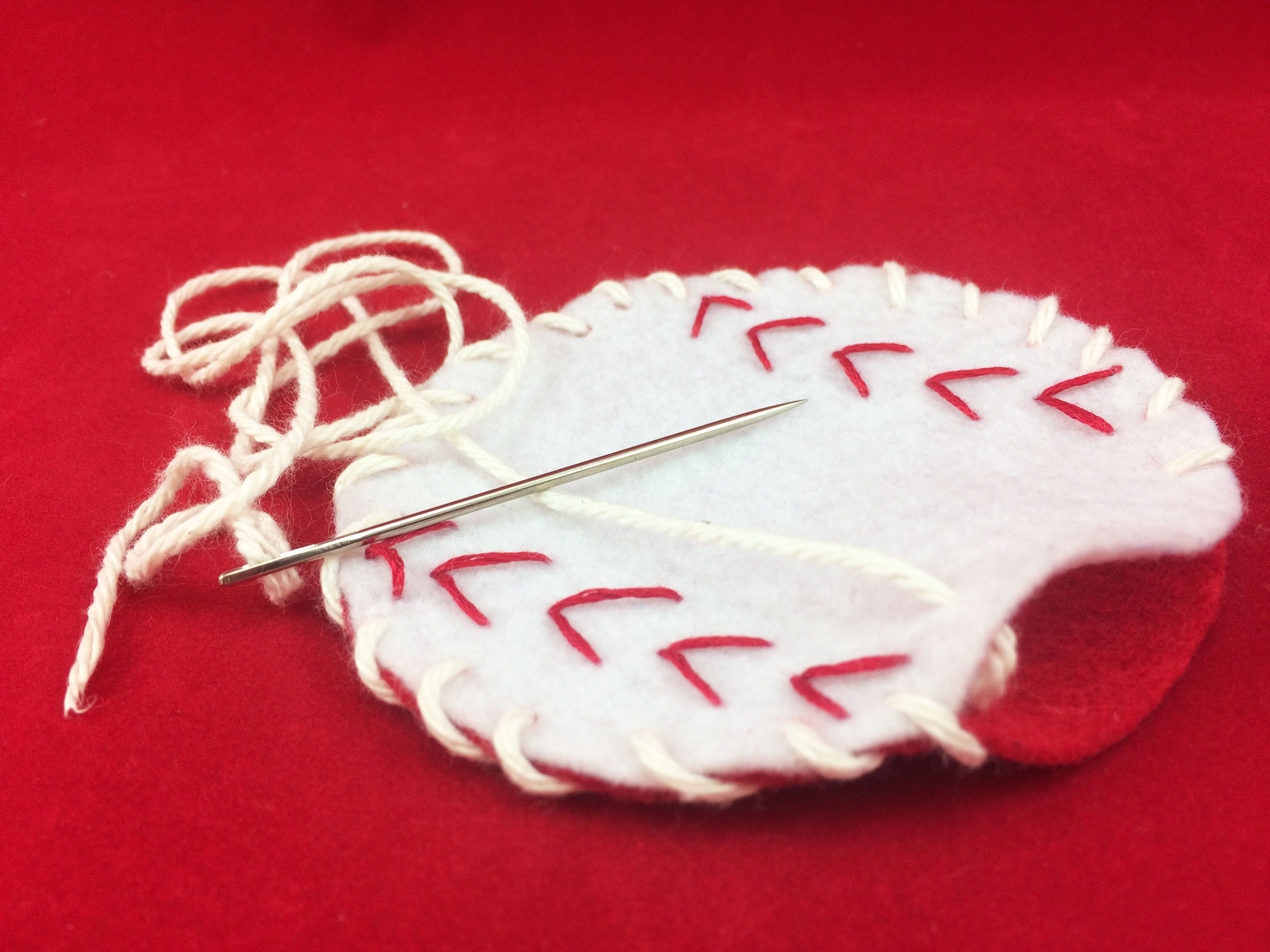 Red felt circle sewn to the back of white baseball with white string. | OrnamentShop.com