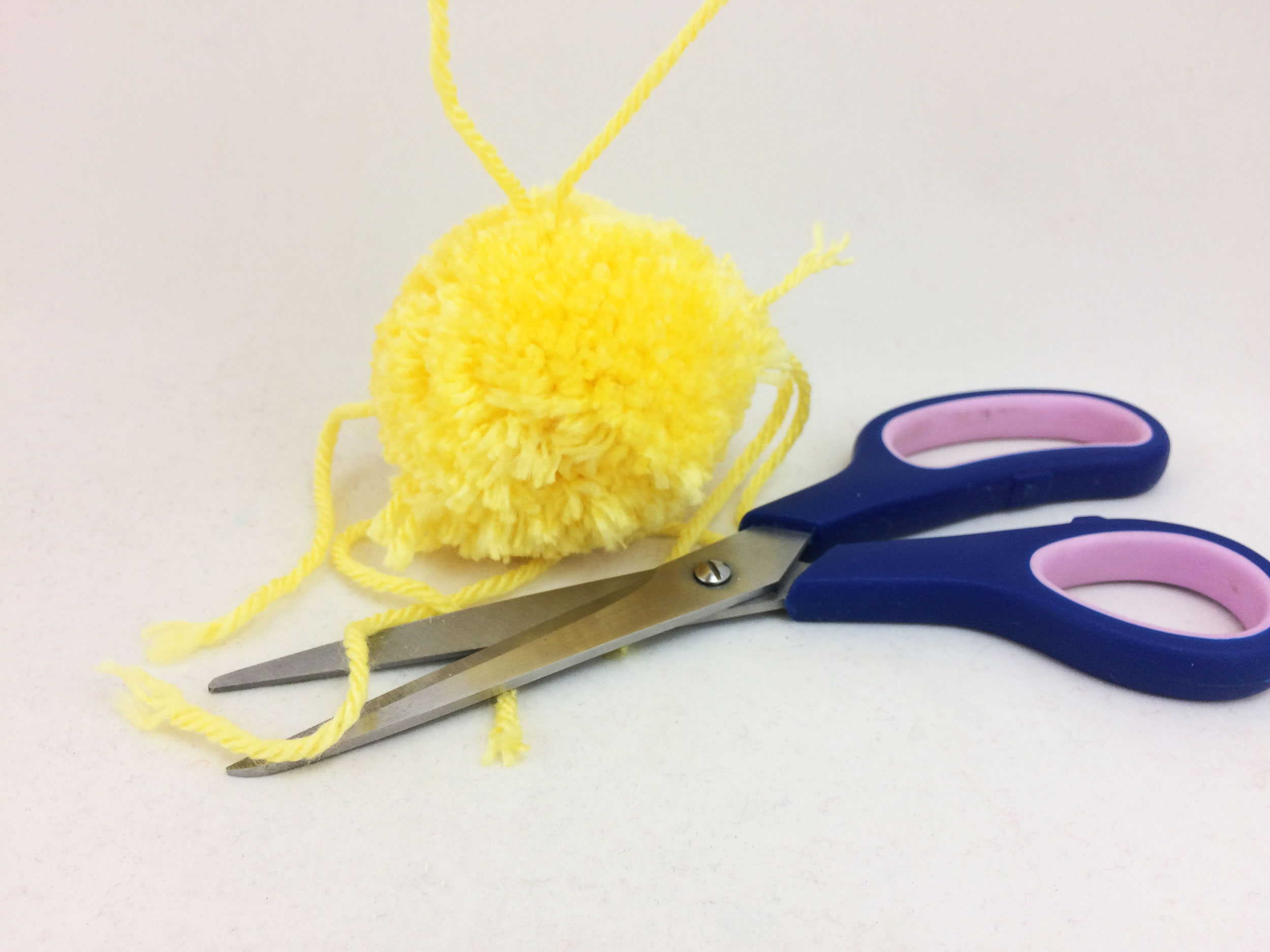Trim excess strings from pom poms and tie loop for DIY Easter Chick Ornament. | OrnamentShop.com