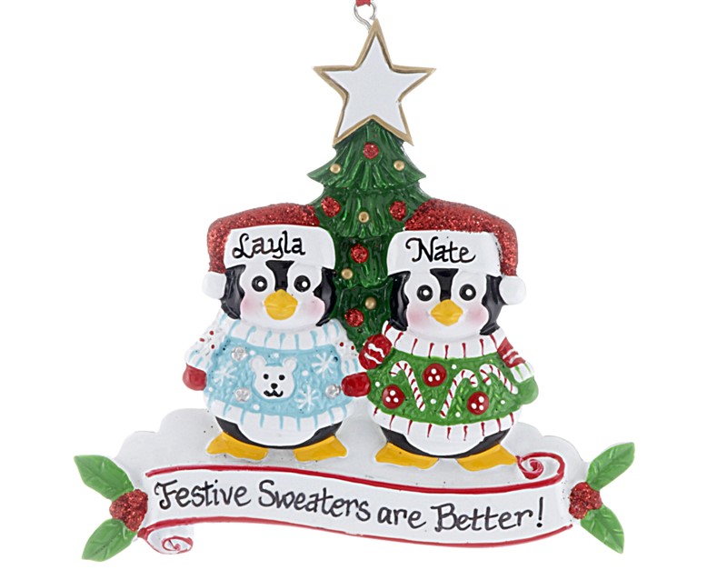 Two penguins stand in front of a Christmas tree personalized with names wearing sweaters. | OrnamentShop.com